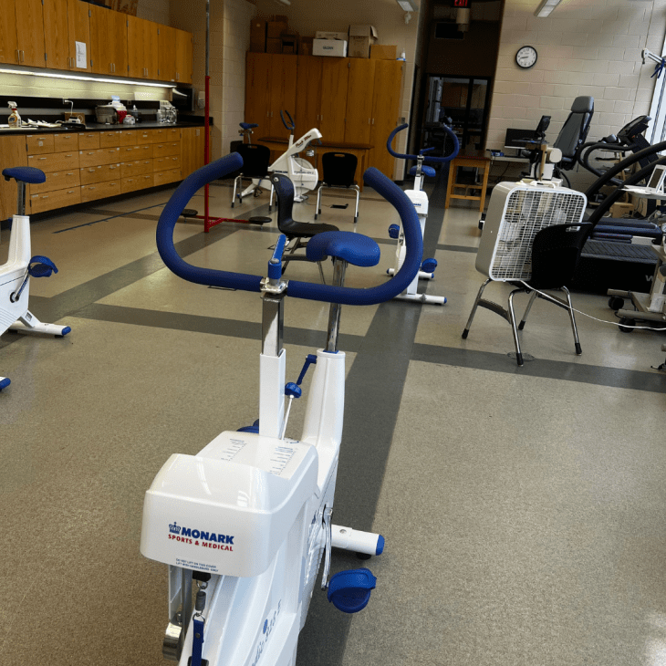 Stationary exercise bikes and fitness testing equipment are set up inside a research lab with cabinets, chairs, and workout machines.