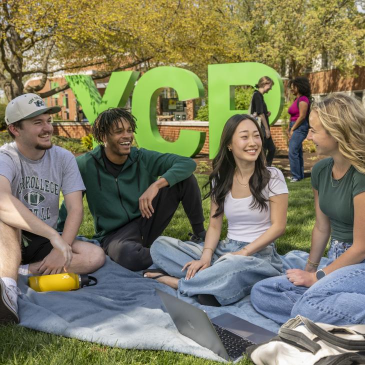 A group of students sitting on the lawn in front of the YCP letters.