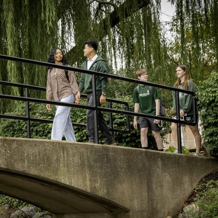 Students walking across the bridge with willow trees behind them.