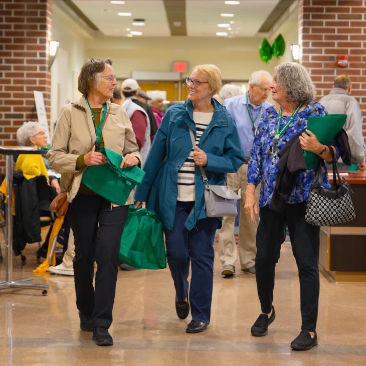 Three Lifelong Learning Initiative participants walk through a York College campus hallway while talking and carrying green program bags.
